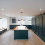 Full shot of kitchen, lighting island, orange chairs and bespoke cupboards.