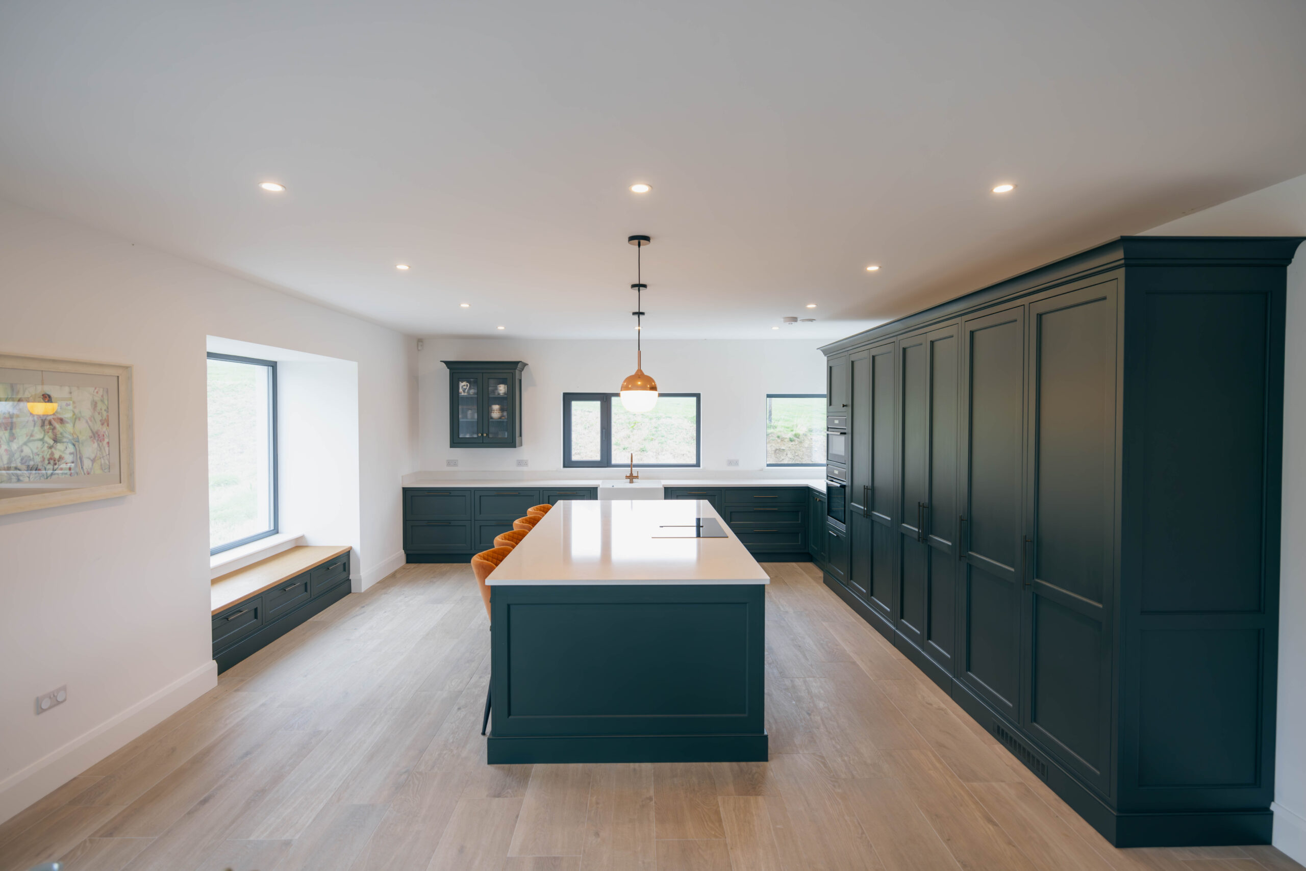Full shot of kitchen, lighting island, orange chairs and bespoke cupboards.